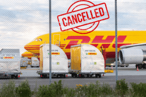 Avión de carga DHL en pista con contenedores, acompañado de un símbolo de cancelado que representa la suspensión de envíos hacia Estados Unidos.