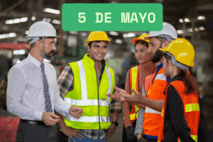 Grupo de obreros conversando junto a un letrero que indica «5 de Mayo», en un entorno laboral