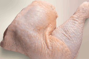 Fotografía de un pedazo de pollo crudo sobre una tabla de cocina, representando el producto avícola cuya importación ha sido suspendida por México debido a un brote de gripe aviar H5N1 en Brasil.