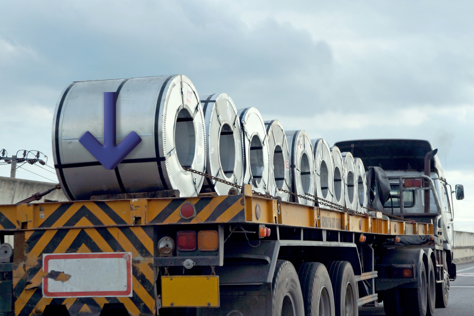 Tráiler de carga transportando acero sobre una autopista mexicana hacia Estados Unidos, con cielo nublado al fondo.